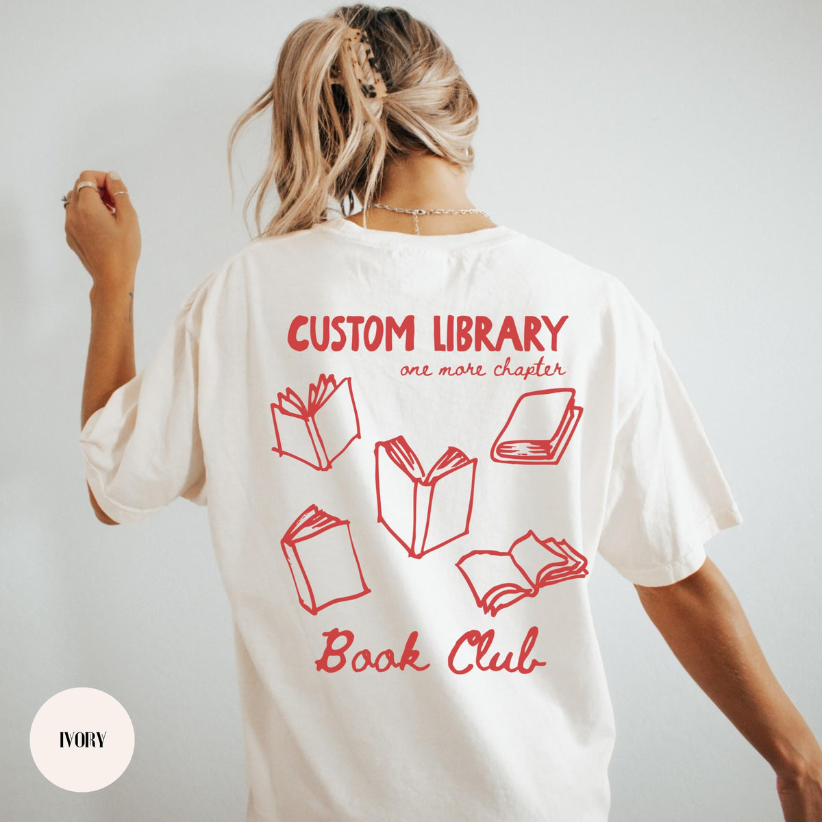 Woman wearing a white custom book club shirt with a red personalized library name, BOOK CLUB lettering and open-book back print.