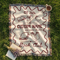 Personalized cream woven book club blanket with a deep red border, custom club name, open books and fringed edges.