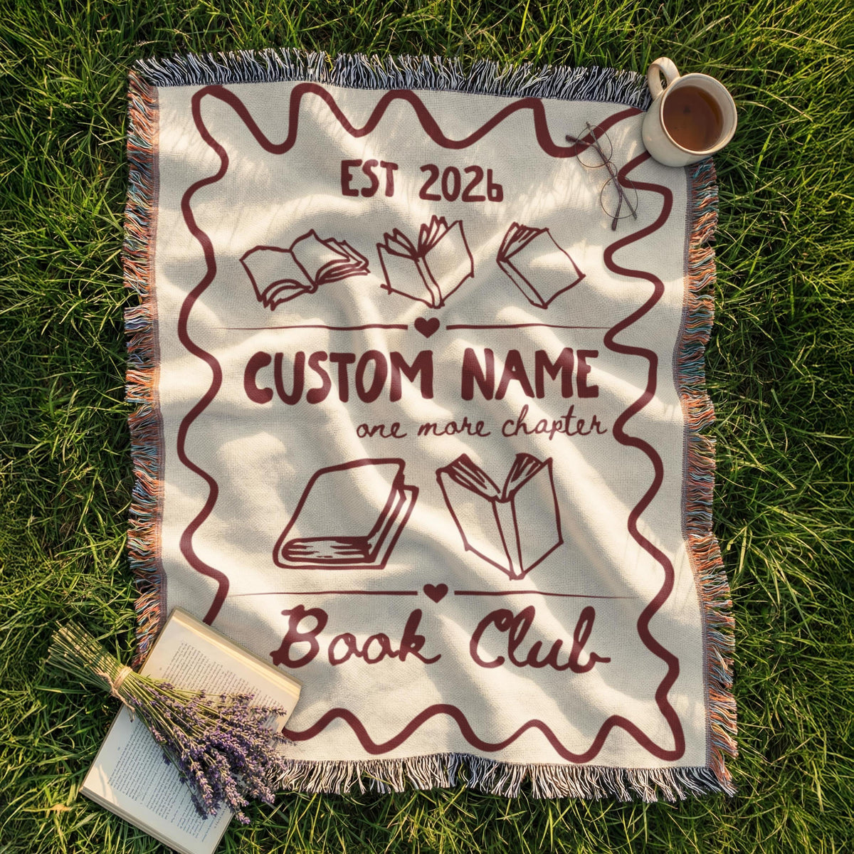 Personalized cream woven book club blanket with a deep red border, custom club name, open books and fringed edges.